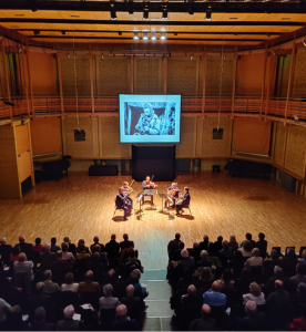 A photo of 5 people playing stringed instruments of smaller-scale chamber music to a crowd.